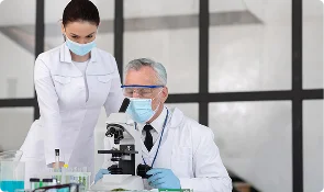 Two masked researchers reviewing a sample under a laboratory microscope, representing mitochondrial research articles