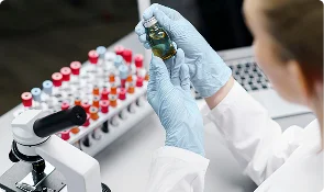 Laboratory researcher holding a sample vial beside a rack of test tubes, representing research context articles